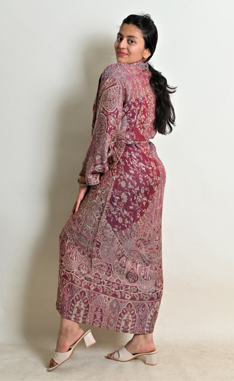 May include: A long, flowing burgundy robe with a paisley pattern. The robe has long sleeves and a matching belt. The model is wearing cream-coloured heeled sandals. The fabric appears to be lightweight and suitable for warmer weather.