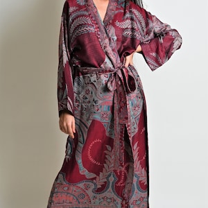 Puede incluir: Larga bata burdeos con estampado de cachemira en tonos turquesa, gris y coral. La bata tiene mangas largas, dise&ntilde;o cruzado y cintur&oacute;n a juego. La tela parece ligera, adecuada para descansar o como prenda de vestir en casa.