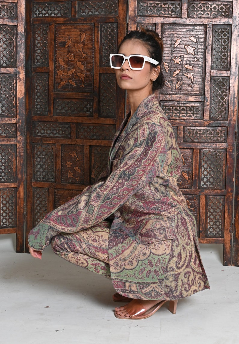 May include: A patterned blazer and matching pants in shades of beige, burgundy, and green. The outfit is worn with white-framed sunglasses. The ensemble is a stylish, coordinated look.