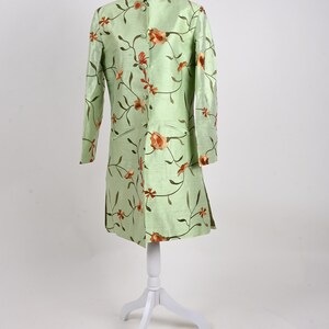 May include: A light green, long-sleeved coat with a mandarin collar and floral embroidery. The coat is displayed on a white mannequin. The floral design features orange and brown flowers and vines.