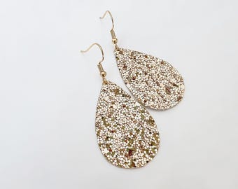 May include: A pair of gold teardrop-shaped earrings with a sparkly glitter finish.