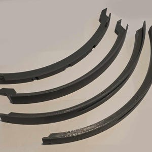 May include: Four dark gray, curved, plastic pieces. Each piece has a unique shape with a flat, rectangular end and a curved body. The pieces are arranged in a fan-like pattern, with the ends pointing in different directions.