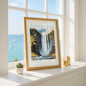 May include: A framed art print featuring the Sk&oacute;gafoss waterfall in Iceland. The artwork depicts the waterfall cascading down a cliff, with the text "SK&Oacute;GAFOSS" at the top and "ICELAND" at the bottom. The frame is a light brown color.