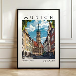 Peut inclure: Une affiche encadrée représentant une scène de rue à Munich, en Allemagne. L'œuvre d'art montre une illustration détaillée de bâtiments et d'une haute tour sous un ciel bleu. Le mot "MUNICH" est en haut, avec "GERMANY" et des coordonnées en bas.