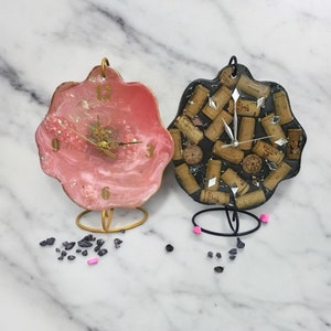 May include: Two resin clock designs with a black and white cork design and a pink and white resin design. Both clocks have gold hands and numbers.