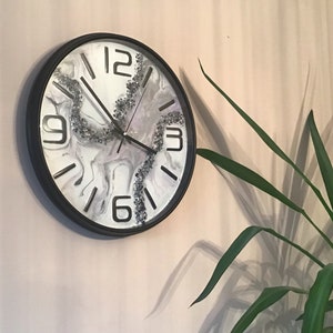 May include: A black and white clock with a marble-like design and silver glitter accents. The clock has black hands and black Roman numeral markings.