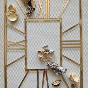 May include: A gold-coloured metal frame with a geometric design. The frame is surrounded by dried flower petals in shades of brown and white.