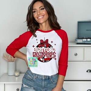 May include: A white and red raglan shirt with the text "Glenrose Beavers" in a disco ball design. The shirt has red sleeves and a white body. The design includes a red bow and stars.