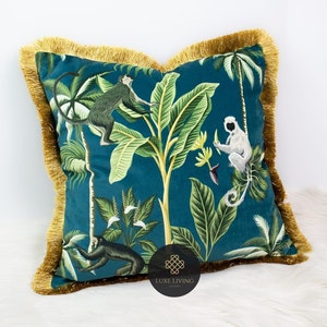 May include: Teal blue velvet cushion with a gold fringe border. The cushion features a tropical print with monkeys, palm trees, and banana leaves.