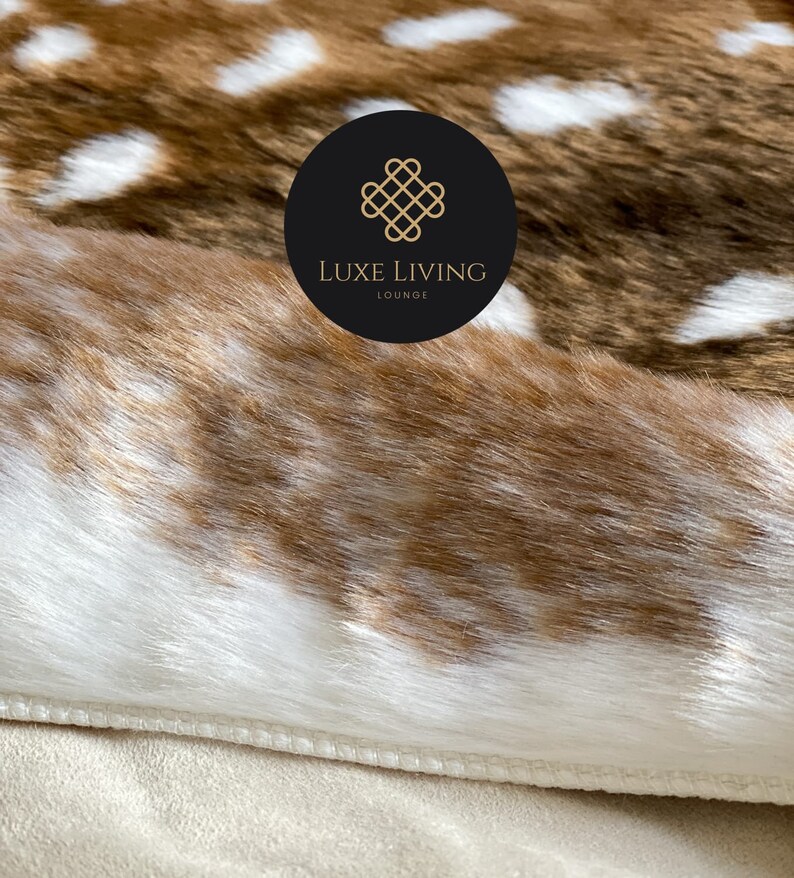 May include: Close-up of a brown and white faux fur rug with a stitched edge. The rug has a pattern of white spots on a brown background. A black circle with a gold logo that says "LUXE LIVING LOUNGE" is visible in the upper right corner of the image.