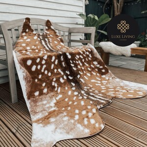 May include: A brown and white faux fur rug with a spotted pattern, resembling a deer hide. The rug is draped over a wooden bench and is on a wooden deck.