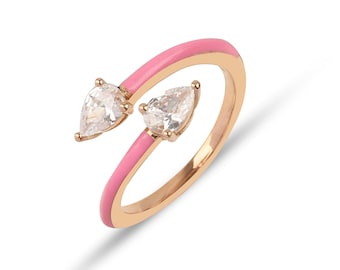 May include: A pink enamel ring with two pear-shaped clear stones.