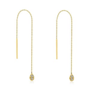 May include: A pair of gold-coloured threader earrings. Each earring has a straight bar at the top, a delicate chain, and a teardrop-shaped charm with small, clear stones at the bottom. The earrings are set against a white background.