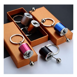 May include: Four different coloured keychains with a gear shift design. The keychains are silver, gold, pink, and blue. Each keychain is in a small box.