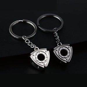 Può includere: Due portachiavi argentati con un design a motore rotativo. Un portachiavi è argentato e l'altro è nero.