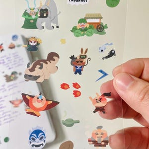 May include: A clear sticker sheet featuring colorful cartoon illustrations of characters and elements from a popular animated series. The sheet includes images of a bison, a cabbage merchant, and the text "MY CABBAGES".