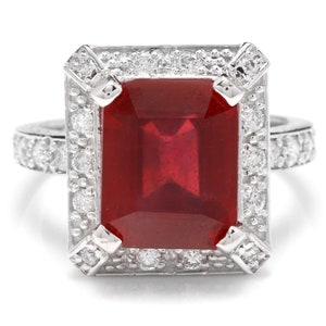 May include: A silver ring with a large, red, emerald-cut gemstone surrounded by a halo of smaller, white gemstones.