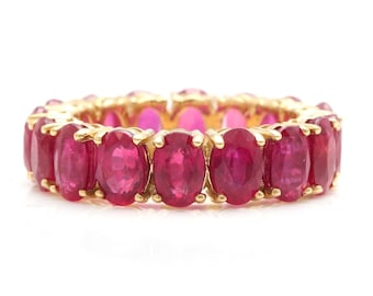 May include: A gold band ring set with a row of oval-shaped ruby gemstones.