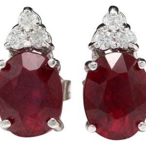 May include: A pair of ruby and diamond earrings. The earrings feature oval-shaped red rubies set in a silver setting. Each ruby is surrounded by three small diamonds.