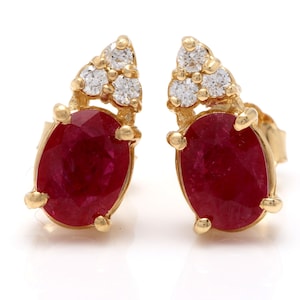 May include: A pair of gold earrings with oval ruby gemstones and diamond accents.