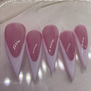 May include: Set of six pink and white stiletto false nails. The nails have a white tip and a pink base.