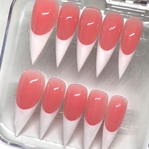 May include: A set of ten stiletto-shaped press-on nails arranged in a clear plastic storage case. Each nail features a glossy, translucent pink base transitioning into a solid white French tip, creating a classic two-tone design with a sharp point.