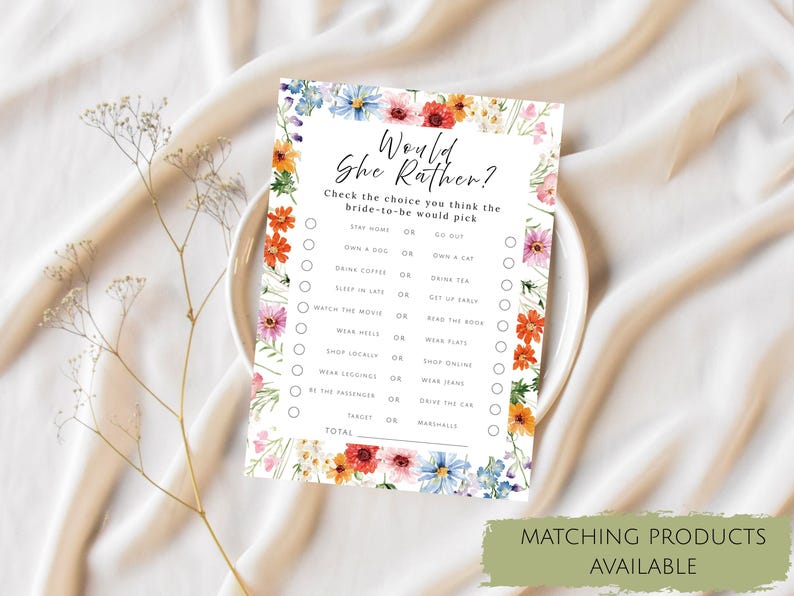 May include: A rectangular game card titled Would She Rather with a floral border of colorful wildflowers. The text includes a list of choices for a bride-to-be, such as stay home or go out, own a dog or a cat, drink coffee or tea, and shop locally or online.