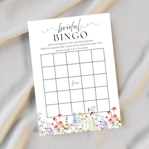 May include: A white "Bridal Bingo" game card with a floral border. The card features a grid for game play and instructions. The text includes "Bridal Bingo", "Fill in the squares with your best guesses", and "First person to get 5 in a row wins!"