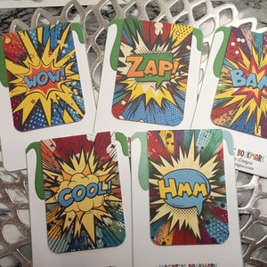 Puede incluir: Un conjunto de cinco marcadores magnéticos con gráficos de estilo cómic. Cada marcador presenta una palabra de acción diferente: "WOW!", "ZAP!", "BAM!", "COOL!" y "Hmm!". Los marcadores tienen un fondo blanco con una pestaña verde.