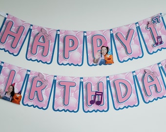 Puede incluir: Bandera rosa y azul con las palabras "HAPPY BIRTHDAY" y "1st". La bandera tiene un diseño de burbujas e incluye imágenes de una persona y un títere. También se presentan notas musicales y bloques ABC.