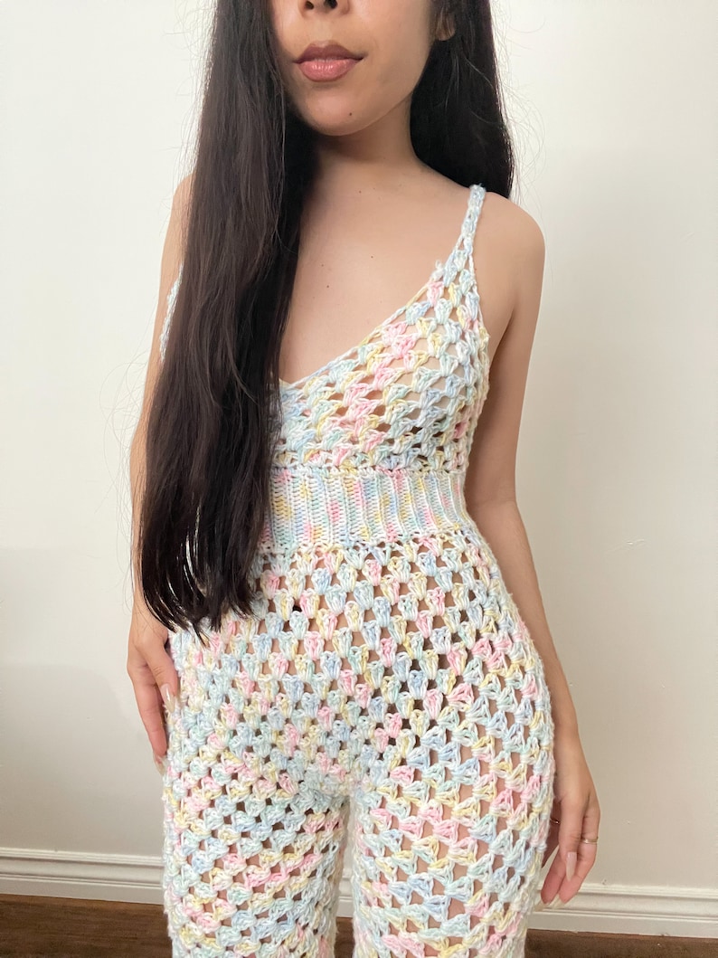 May include: A pastel-colored crochet jumpsuit with a loose-fitting, flowy design. The jumpsuit features a V-neckline and thin straps.