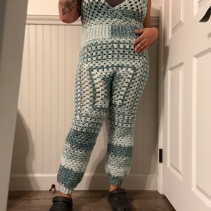 May include: A crocheted jumpsuit in shades of blue and white. The jumpsuit has a wide leg and a V-neckline. The person is wearing black clogs.