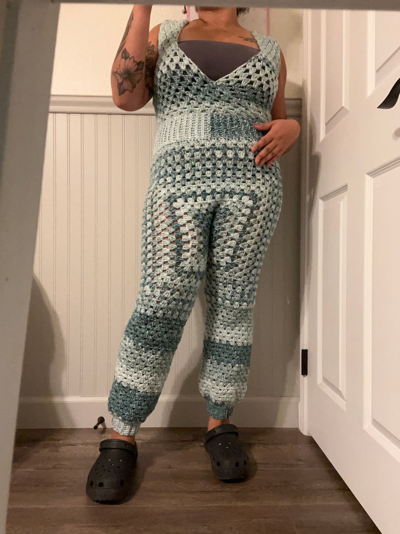 May include: A crocheted jumpsuit in shades of blue and white. The jumpsuit has a wide leg and a V-neckline. The person is wearing black clogs.