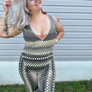 May include: A woman wearing a gray and white crochet maxi dress with a deep V-neckline. The dress has a geometric pattern and is sleeveless.