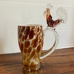 Puede incluir: Una taza de vidrio con un patrón de manchas marrones y blancas y un asa de gallo de vidrio transparente.