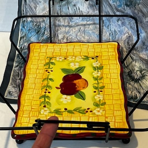 Peut inclure: Un plat en céramique jaune avec un motif tissé et un motif de pomme rouge et verte. Le plat est dans un support en métal noir.