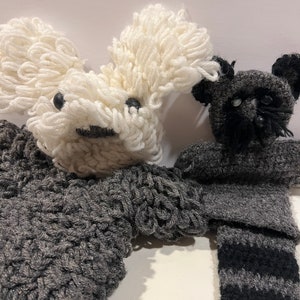 May include: Handmade crochet stuffed animals. One is white with black eyes and a gray mouth, the other is black and gray. The body of the white animal is gray. The black and gray animal has a striped tail.