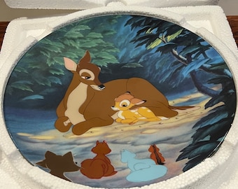 May include: A ceramic plate with a scene from the Disney movie Bambi. The plate features Bambi, his mother, and three other woodland creatures. The plate is decorated with a blue and green forest background.