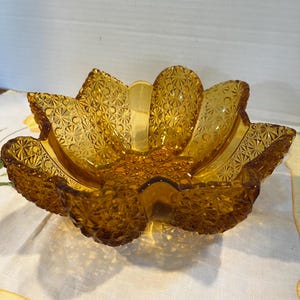 May include: A vintage amber glass bowl with a flower-shaped design. The bowl has a textured surface with a repeating pattern of small circles.
