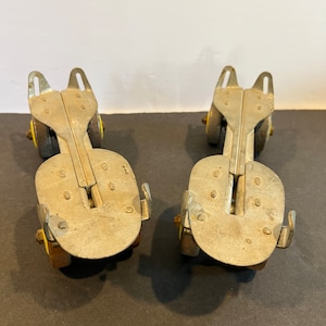 May include: A pair of vintage metal roller skate attachments with yellow wheels. The skates are silver and have a simple design.