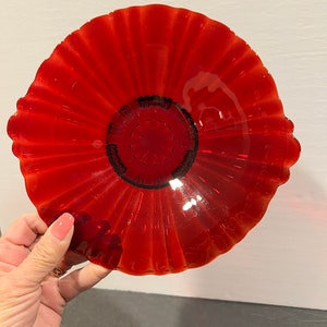 May include: A red glass dish with a scalloped edge and a smaller, circular dish in the centre. The dish is made of clear glass with a red tint.