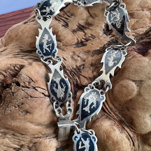 May include: A silver bracelet with black enamel and a repeating design of a stylized figure. The bracelet is made of linked oval-shaped pieces with a decorative edge.