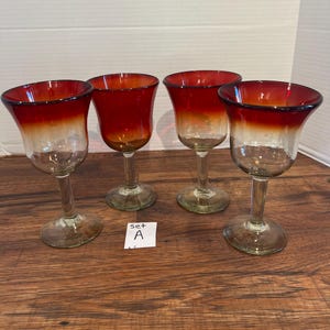 Op de afbeelding: Set van vier rode en heldere glazen wijnglazen met een ombre-effect. De glazen staan op een houten oppervlak met een wit briefje waarop "Set A" staat.