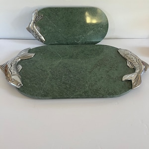May include: Two green marble serving platters with silver fish accents. The oval-shaped platters have a polished finish and are decorated with detailed fish at each end. A decorative and functional addition to any kitchen or dining room.