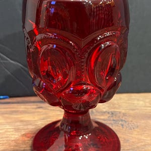 Op de afbeelding: Een diep rood glazen kelk met een getextureerd, stervormig patroon. De kelk heeft een brede voet en een lange, slanke steel.
