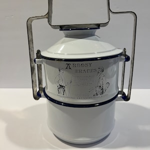 Op de afbeelding: Een witte emaille lunchbox met een blauwe rand en een metalen handvat. De lunchbox heeft een gedrukte afbeelding van twee mannen met bretels en de tekst "Argosy Braces" en "Give the Argosy a Trial". De lunchbox heeft ook de tekst "Central Wholesale Depot 6 & 7 Newgate Street, Boston".