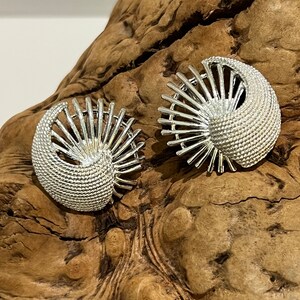 May include: A pair of silver earrings with a geometric design. The earrings are shaped like a fan and have a textured surface.