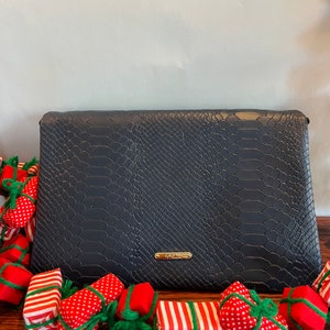 May include: A black snakeskin clutch purse with a gold logo. The purse is surrounded by a garland of red and white striped, red and white polka dot, and solid red gift boxes tied with green ribbon.