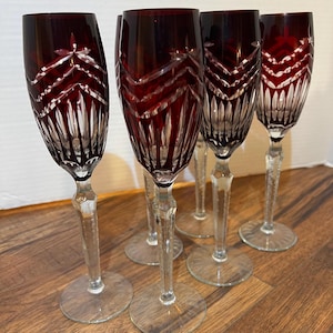 May include: Set of six red crystal wine glasses with a cut glass design. The glasses have a clear stem and base.