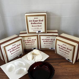May include: An Avon 1876 Cape Cod Collection dessert bowl set. The set includes a dark red glass bowl, white soaps, and boxes with text. The boxes are cream-coloured with brown trim and text.
